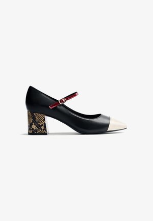 Chaussure Mary Jane noire avec un bout pointu blanc, une bride rouge et un talon chunky en faux serpent marron sur un fond blanc.