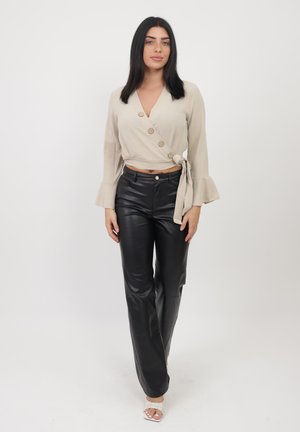 Top avvolgente beige con tre bottoni e maniche a campana; abbinato a pantaloni in pelle neri a gamba stretta e sandali bianchi con fasce.