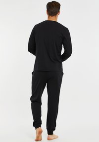 Sort langærmet top med rund halsudskæring og tætsiddende manchetter, parret med matchende sorte joggers med elastiske ankler og sidelommer.