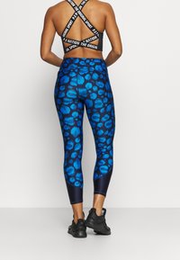 Svart sportbehå med märkesremmar, matchade med blå leopardmönstrade leggings med glansig yta och mörka accenter. Svarta sneakers fulländar looken.