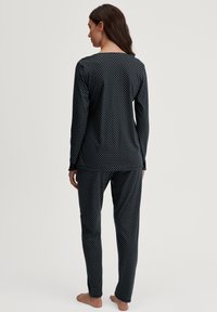 Zwart polkadot pyjama set gemaakt van zachte stof, met lange mouwen en een relaxed fit broek. Opvallend wit stippenpatroon door de gehele set.