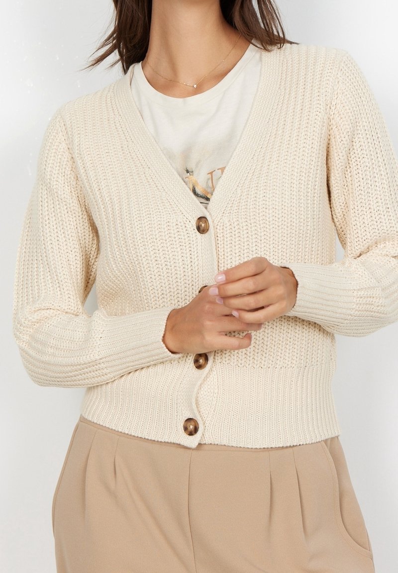 Pletený cardigan v krémové barvě s výstřihem do V, zapínáním na knoflíky, žebrovanými manžetami a lemem. Obsahuje hnědé knoflíky a texturovaný vzor.