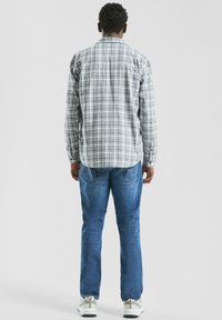 Koszula na długi rękaw w kratę w kolorach białym, niebieskim i zielonym, zestawiona z niebieskimi dżinsami. Model stoi tyłem, prezentując szczegóły i dopasowanie koszuli.