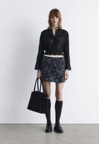 Black cropped blouse with button details, navy textured skirt, knee-high black socks, and a black suede tote bag. Flat black shoes.