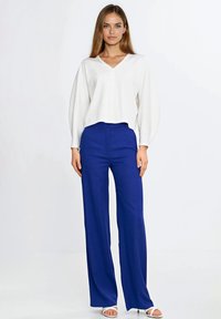 Biała bluzka z dekoltem w serek i długimi, bufkowatymi rękawami, zestawiona z wysokim stanem i szerokimi nogawkami niebieskich spodni. Strój charakteryzuje się eleganckim, minimalistycznym designem.