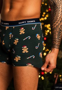 Mörkgröna kalsonger med ett mönster av pepparkaksgubbar och polkagrisar. Resåren är marinblå med texten "HAPPY SHORTS" i vit färg.
