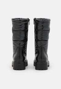 Botas acolchadas negras con acabado brillante, que cuentan con una suela gruesa, cierre de cremallera y acentos laterales texturizados. Talón reforzado para mayor durabilidad.