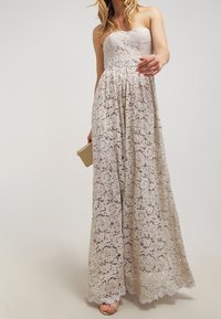 Strapless, floor-length dress in light beige lace with floral pattern and a silver accent at the waist. Smooth, delicate texture.