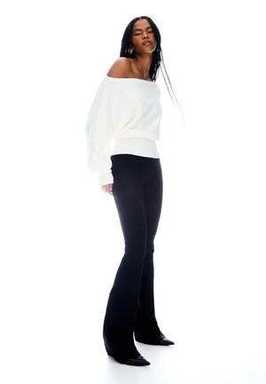 White off-shoulder sweater in soft fabric with wide sleeves, paired with fitted black flared pants. Black pointed-toe heels complete the look.