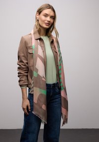 Écharpe légère avec un motif aux couleurs pastel, portée sur une tenue décontractée composée d'un haut vert menthe et d'une veste marron.