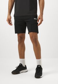 Shorts atletici negri cu logo-ul BOSS, asortați cu adidași negri și șosete albe. Shorts-urile au un design ajustat și o textură de țesătură netedă.