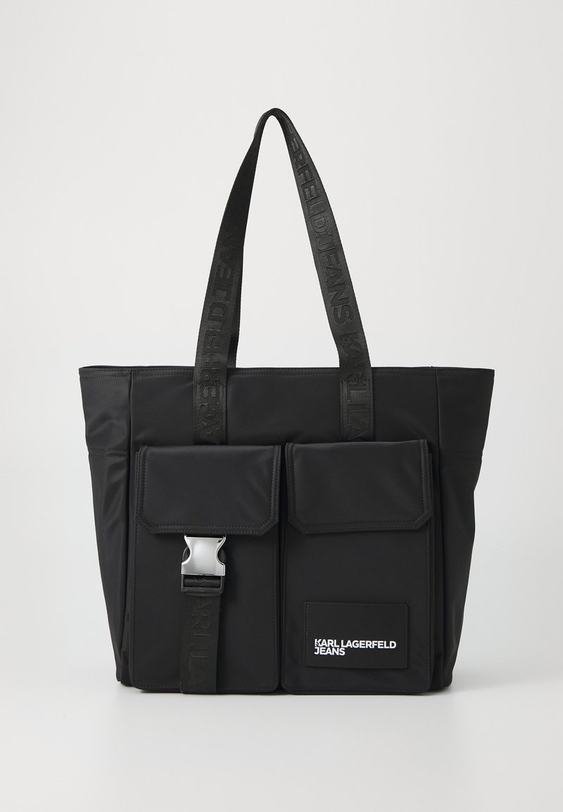 Melnas neilona soma ar divām priekšējām kabatām, sudraba krāsas sprādze, arzīmētas tekstilmateriāla plecu siksnas un taisnstūra formas logo uzlīme.