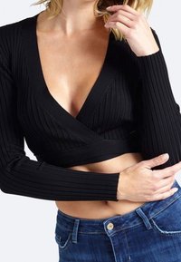 Top corto nero a coste con maniche lunghe e scollatura profonda a V, caratterizzato da uno stile avvolgente e una vestibilità aderente. Abbinato a jeans blu.