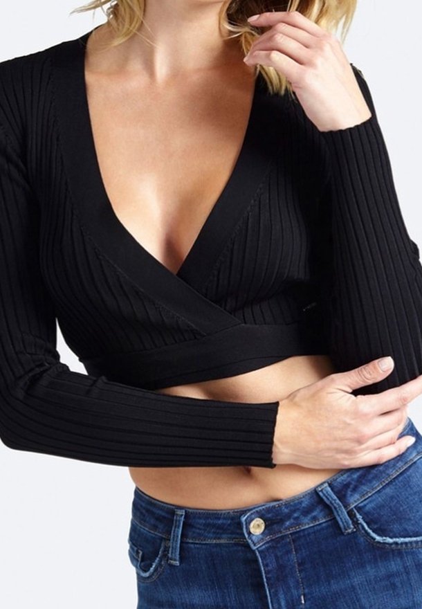 Top corto nero a coste con maniche lunghe e scollatura profonda a V, caratterizzato da uno stile avvolgente e una vestibilità aderente. Abbinato a jeans blu.