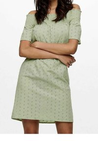 Ljust grön avskuren klänning med korta ärmar, texturerad tyg med ögldetaljer och en figurnära siluett som slutar ovanför knäna.