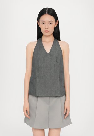 Top grigio a halter con un design incrociato e tessuto testurizzato, abbinato a pantaloni corti plissettati grigio chiaro. Look semplicistico e moderno.