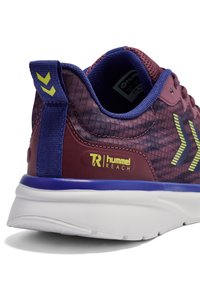 Fioletowo-bordowy but sportowy z teksturowaną cholewką, białą podeszwą i żółtymi akcentami. Posiada tylną pętlę do zakładania oraz logo Hummel.