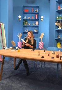 Träbord med olika kosmetiska produkter, inklusive flaskor och burkar. Ljust blå bakgrund med hyllor och dekorativa detaljer.