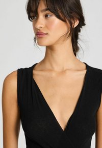 Abito senza maniche nero con scollatura a V profonda, texture del tessuto morbida e silhouette aderente. Presenta un design incrociato a strati sul busto.