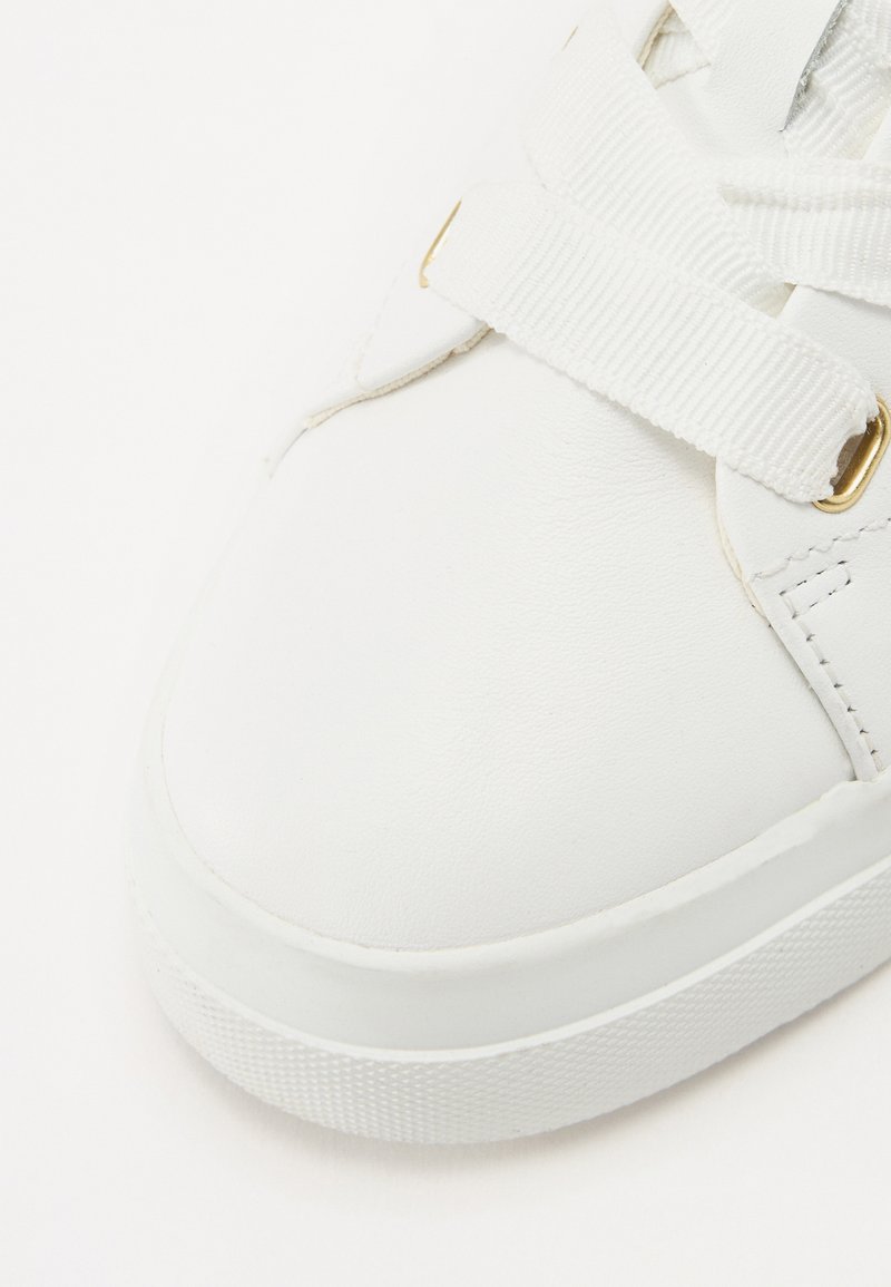 Baskets en cuir blanc avec une surface texturée, dotées de lacets plats blancs, d'œillets dorés et d'une épaisse semelle en caoutchouc.