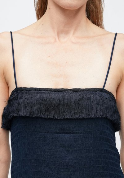 Tengerészkék ruha vékony spagetti pántokkal, texturált teste és a nyakkivágásnál rojtos díszítéssel a részletek fokozására.