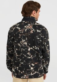 Schwarze und weiße kuschelige Fleecejacke mit abstrakten Mustern in Brauntönen, mit hohem Kragen und langen Ärmeln.