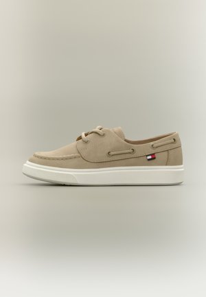 Μπεζ καστόρινες μοκασίνια με λευκές λαστιχένιες σόλες, σχέδιο με κορδόνια και μικρό λογότυπο σε κόκκινο, λευκό και μπλε στο πλάι.