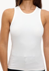 Witte mouwloze top met een ribbelstructuur, aangesloten ontwerp en ronde halslijn, vervaardigd van zacht materiaal voor een comfortabele pasvorm.