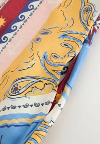 Tissu plié avec des motifs nautiques colorés comprenant des ancres, des vagues et des motifs de soleil dans des tons jaunes, bleus, rouges et blancs.