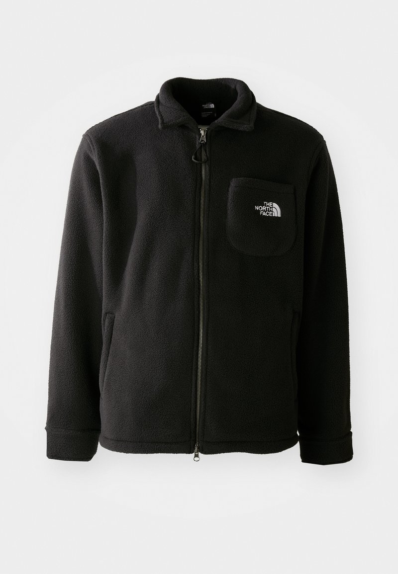 Veste en polaire noire avec fermeture éclair à l'avant, col haut, poignets élastiques et une poche poitrine avec un logo. Texture douce, design décontracté.