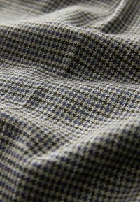 Textil mit einem Hahnentrittmuster in Grau, Marineblau und Beige. Der Stoff hat eine weiche Textur und wird drapiert mit sichtbaren Falten gezeigt.
