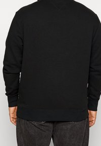 Černá mikina s dlouhými rukávy a žebrovanými manžetami a lemem, s jednoduchým designem bez viditelných log nebo vzorů.