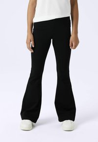 Schwarze ausgestellte Hose aus dehnbarem Material mit einem hoch taillierten Design. Kombiniert mit weißen Sneakers für einen lässigen Look.