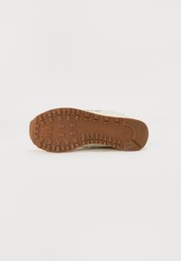 Semelle d'une basket avec des crampons profonds et à motifs en caoutchouc marron sur fond blanc, montrant le design de traction et le logo de la marque.