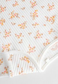 Weißer gerippter Stoff mit einem floralen Muster in Pink, Orange und Braun. Enthält einen weichen, abgerundeten Ausschnitt und ein Markenetikett am Rand.
