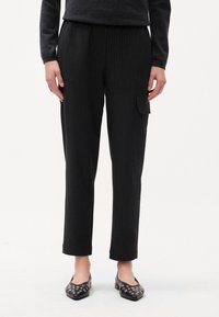 Pantalon noir à rayures avec une coupe décontractée, doté d'une taille élastique et d'une poche latérale pour plus de praticité. Texture de tissu lisse.