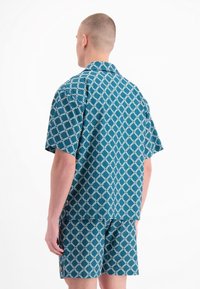 Kortekleurige shirt met korte mouwen en shorts van turquoise stof met een wit geometrisch patroon, met een relaxte pasvorm en kraag.