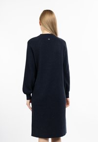 Marineblaues gestricktes Kleid mit langen Ärmeln, lockerer Passform und rundem Ausschnitt, das über den Stoff hinweg dezente Sprenkel aufweist.