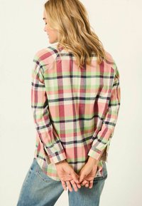 Plaid shirt in pink, green, and white hues, featuring long sleeves, button cuffs, and a relaxed fit, paired with denim pants.