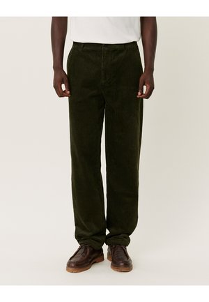 Groene corduroybroeken met verticale ribben, rechte snit en een ritssluiting. Ggedragen met bruin leren schoenen met een gestructureerde afwerking.