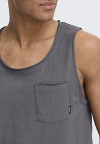 Graues Tanktop aus Baumwolle mit rundem Ausschnitt, einer Brusttasche auf der linken Seite und einem kleinen Markenetikett am unteren Saum.