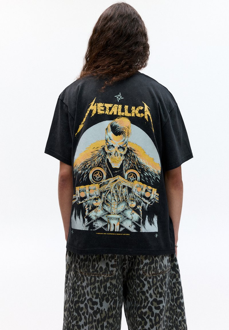 Černé bavlněné tričko s velkým grafickým potiskem lebky s kožešinovými akcenty a kovovými prvky. Tučný text "Metallica" nahoře.