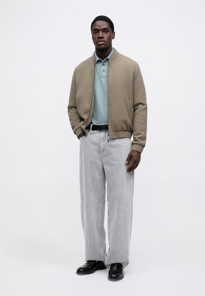 Μαύρη μπομπέρ ζακέτα πάνω από ένα ανοιχτό μπλε πόλο, σε συνδυασμό με ανοιχτό γκρι παντελόνι σε φαρδιά γραμμή και μαύρα παπούτσια. Απλός σχεδιασμός, υφασμάτινη υφή, ελάχιστες λεπτομέρειες.