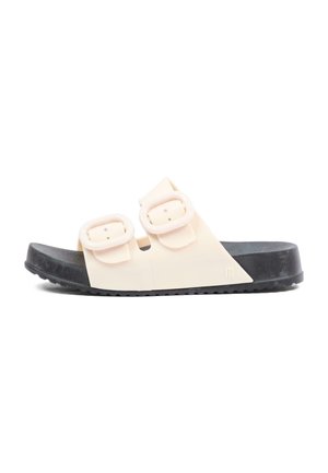 Sandale slide beige unique avec deux boucles réglables et une semelle noire texturée, vue de côté sur fond blanc.