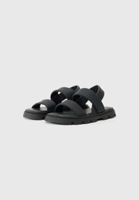 Mustad mustriga ja kummist materjalist mustad ristsanga sandaalid, avatud varvastega disain, paks tekstureeritud tallaga ja mustriga detail, mis tagavad haardumise ja toe.