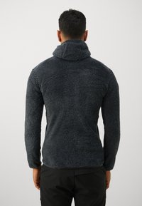 Tmavohnedý fleece pulóver s vysokým golierom a textúrovaným povrchom. Má dlhé rukávy a voľný strih, vhodný na každodenné nosenie.