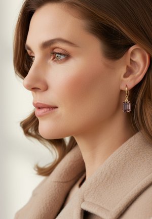 Gouden oorbellen met een rechthoekige paarse edelsteenhanger, gedragen door een vrouw met middellang bruin haar en een beige jas. Gladde huidtextuur.