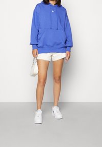 Blå bomulls-huvtröja med framficka och vitt Nike-logotyp, kombinerad med vita shorts och vita sneakers. Lätt och avslappnad design.