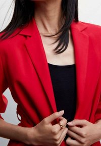 Blazer rojo entallado con solapas con muesca, de tela ligera. Llevado sobre una camiseta de tirantes negra, con textura suave y silueta ajustada.