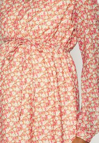 Vestido floral com tecido leve, padrões em rosa, branco e verde; cintura elástica e mangas compridas com detalhes franzidos.